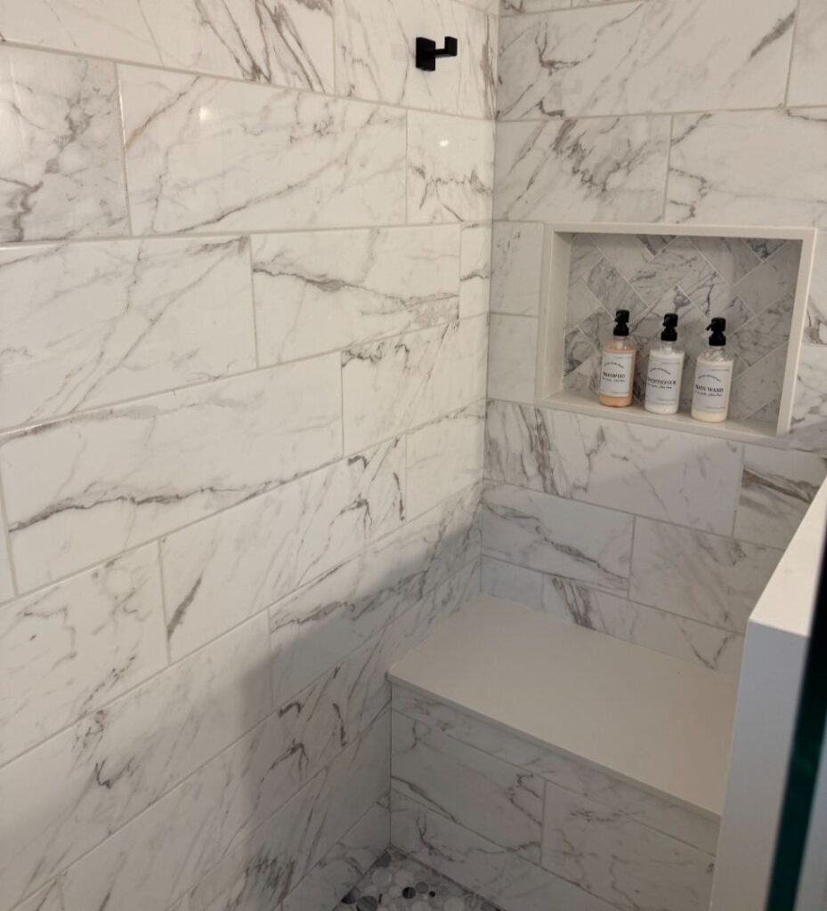 Modern shower gallery with marble tile, built-in bench, and niche with toiletries.