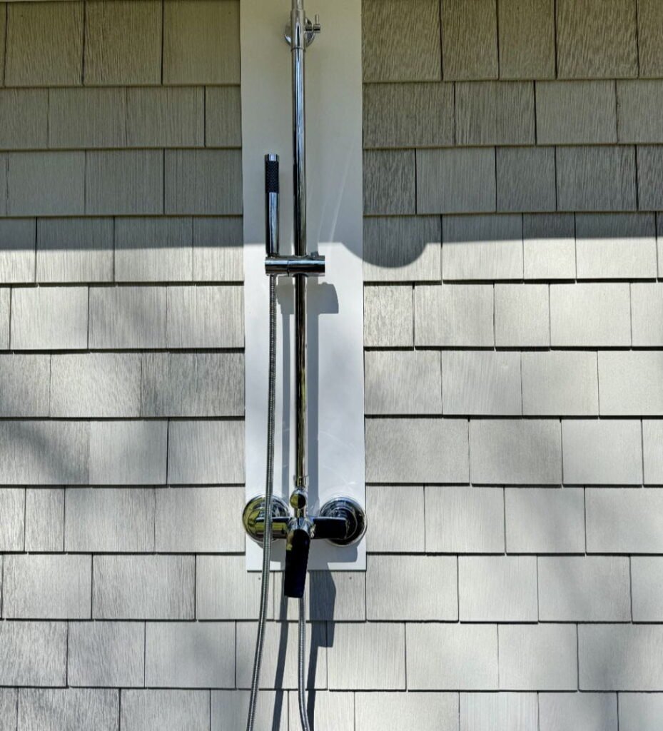 Outdoor shower fixture mounted on a grey shingle wall.