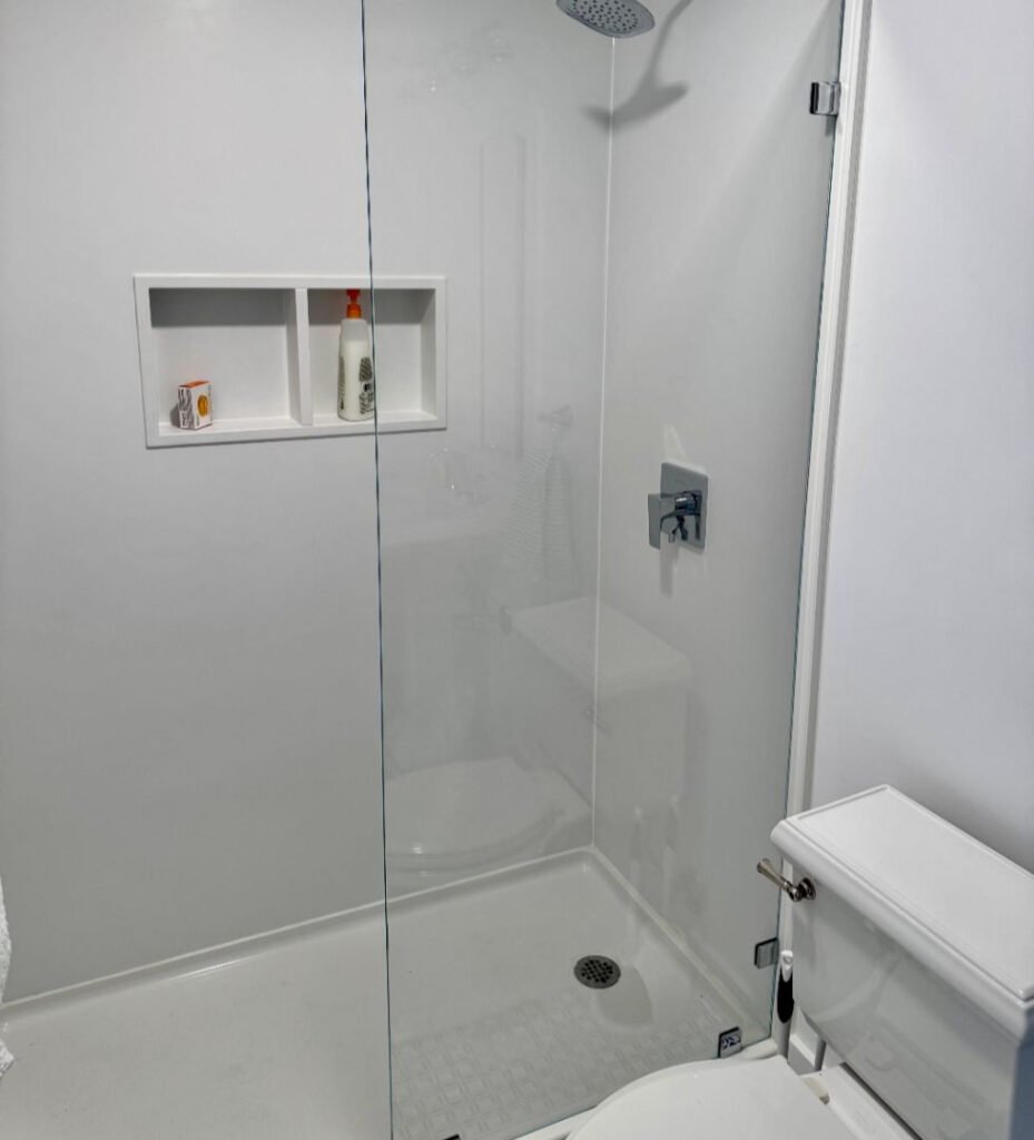 Modern white shower stall with glass door and recessed shelves in a bathroom gallery.