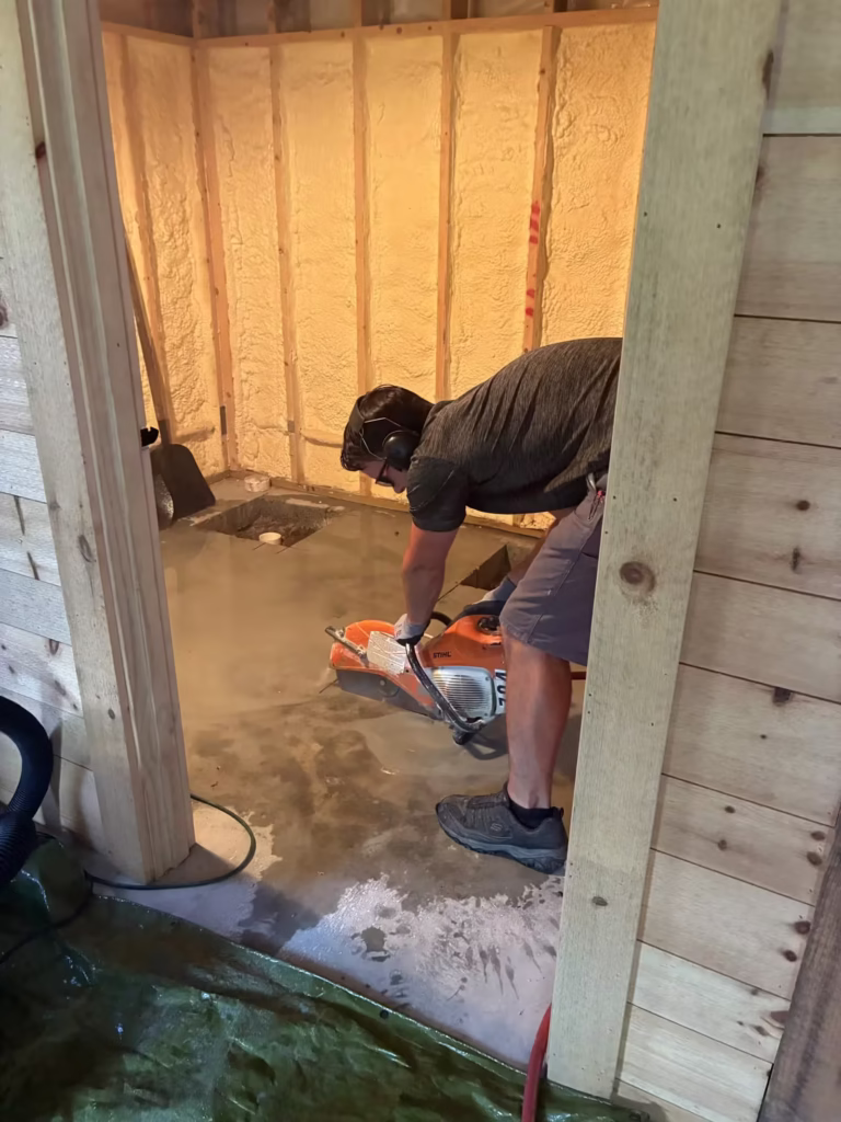 Man cutting concrete floor with a saw, possibly for plumbing work.