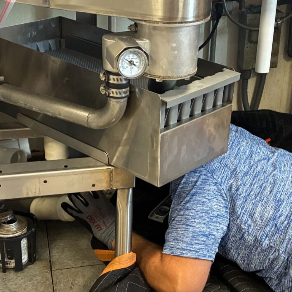 Plumber working under a sink with plumbing and equipment.