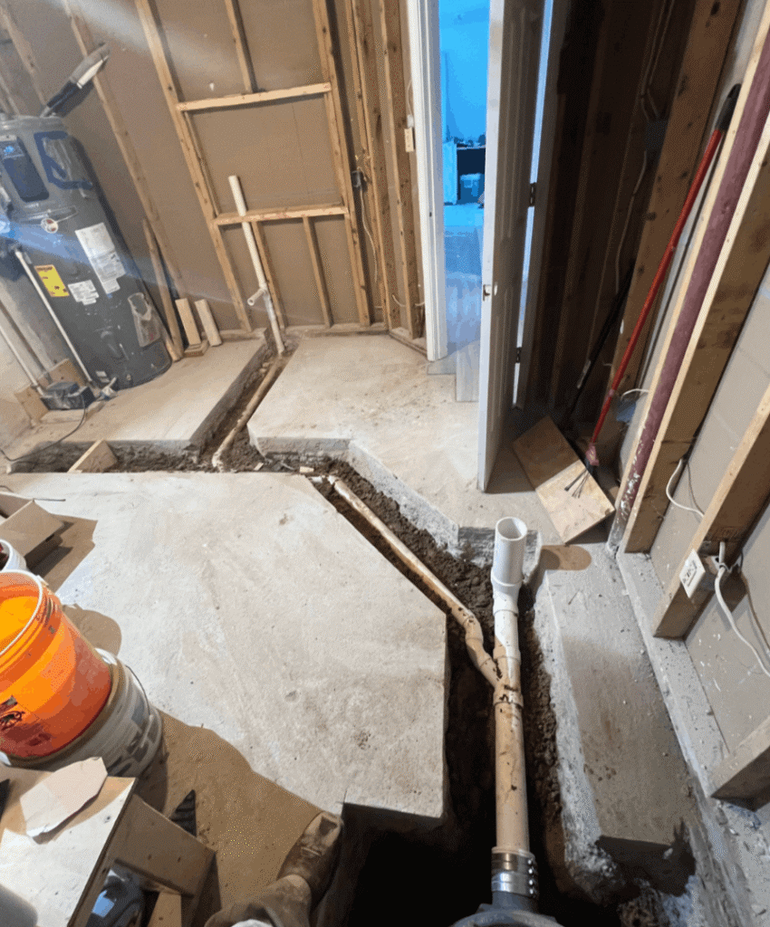 Plumbing rough-in for a bathroom remodel, showing pipes in concrete.